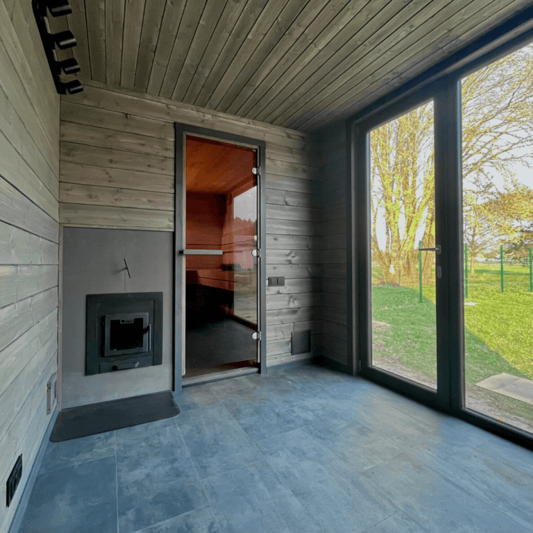 Sauna module anteroom with a wood stove, tiled floor and a corner window to the garden