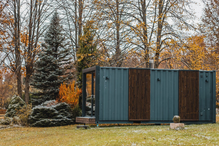 Container sauna module with wood slat panels and a chimney in a garden in late autumn