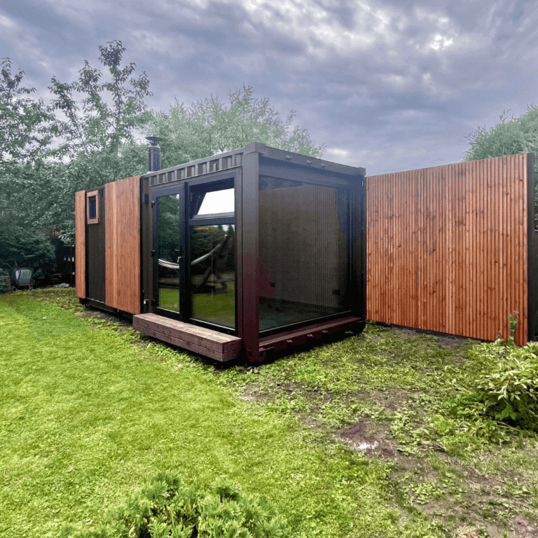 Container sauna module with wood cladding, glass front and a small deck in a garden