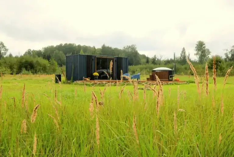 Lote shipping container cabin with a wooden deck and a hot tub in a meadow at the edge of a forest